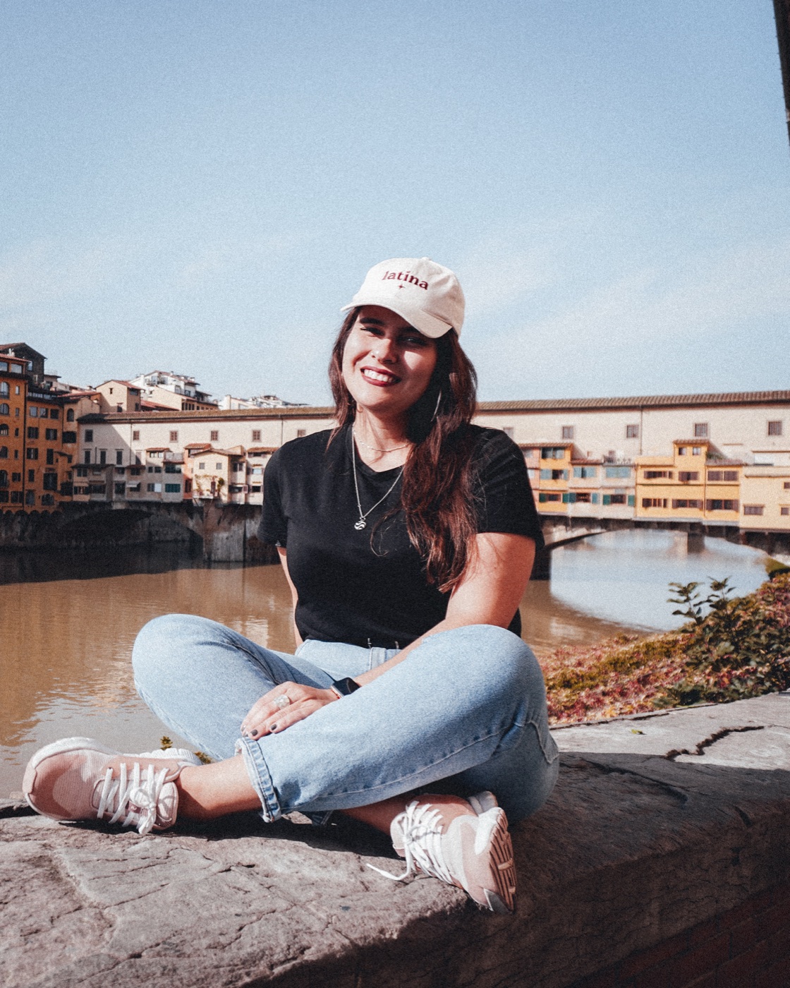 Anna sentada sorrindo, com uma ponte e o rio atrás